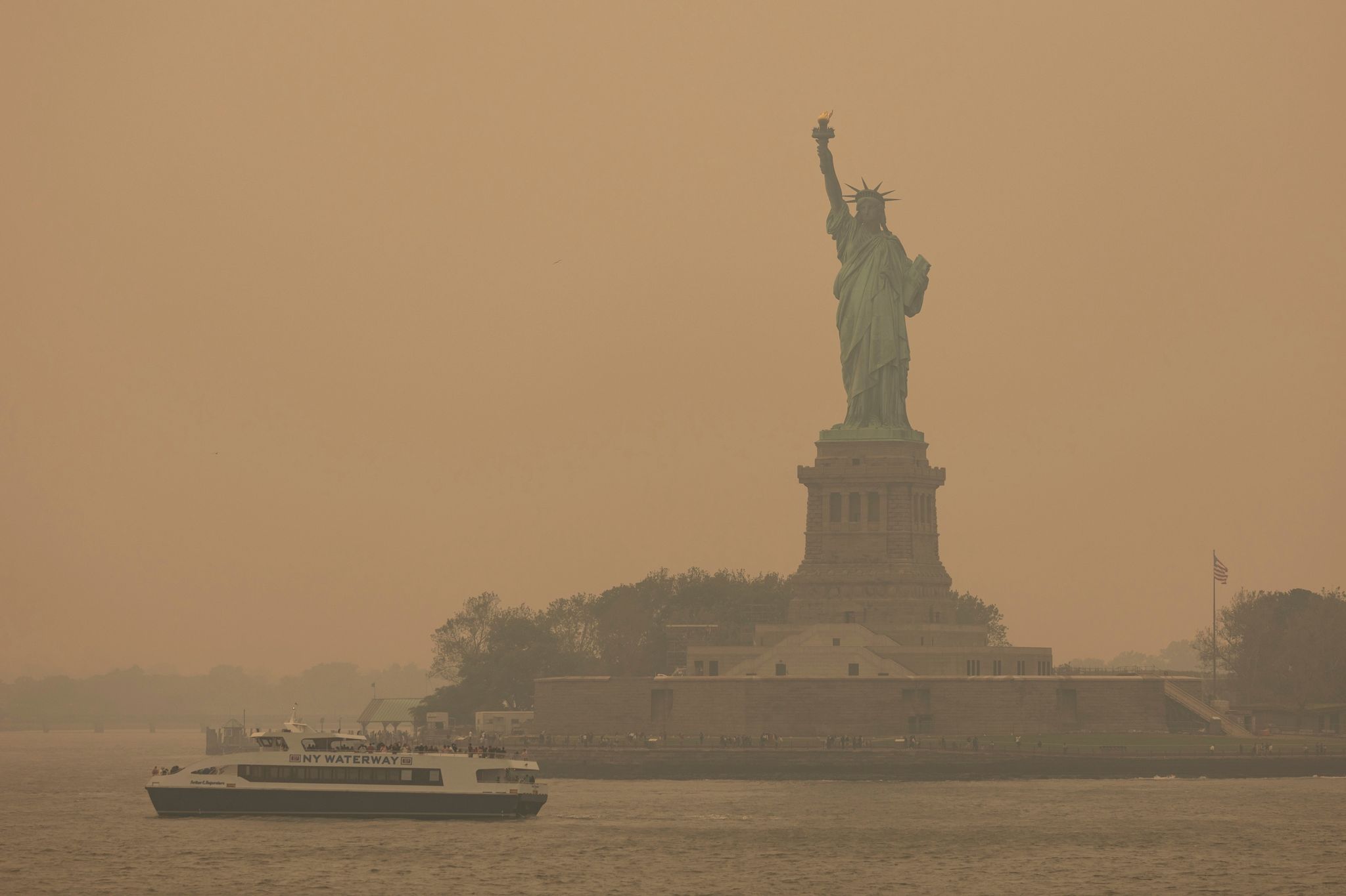 Die Freiheitsstatue ist in orangefarbenen Dunst gehüllt. Foto: Yuki Iwamura/AP/dpa