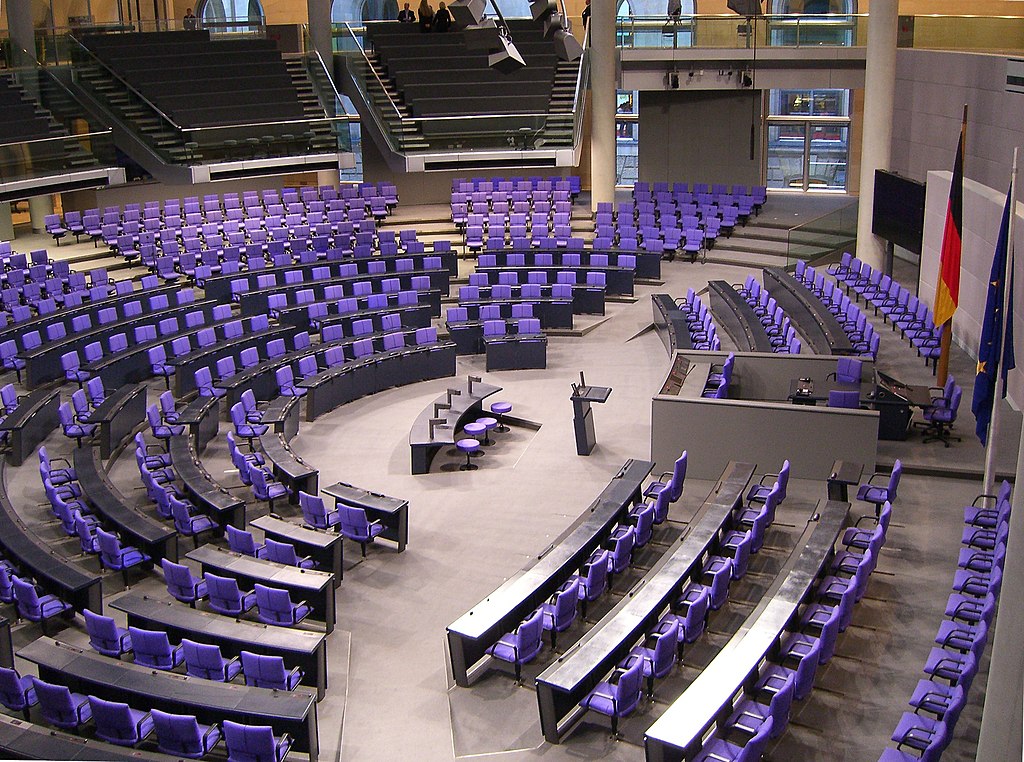 Deutscher Bundestag Plenarsaal Seitenansicht by Times is licensed under CC BY-SA 3.0.