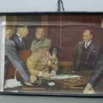 [Bild: Museum of World War II Boston Natick Massachusetts 2015. Munich Agreement artefacts, wall board with coloured photograph of Hitler signing by Lee Wright / CC BY 2.0 / https://creativecommons.org/licenses/by/2.0/]